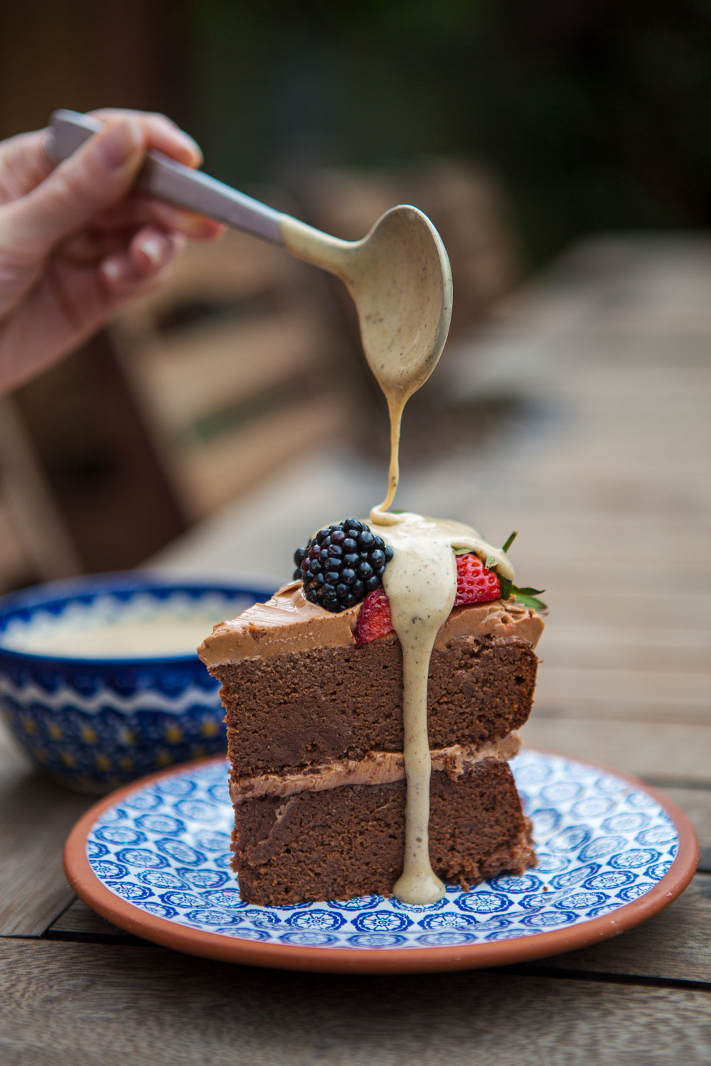 Slice of chocolate cake with berries being drizzled with cream on a decorative plate.