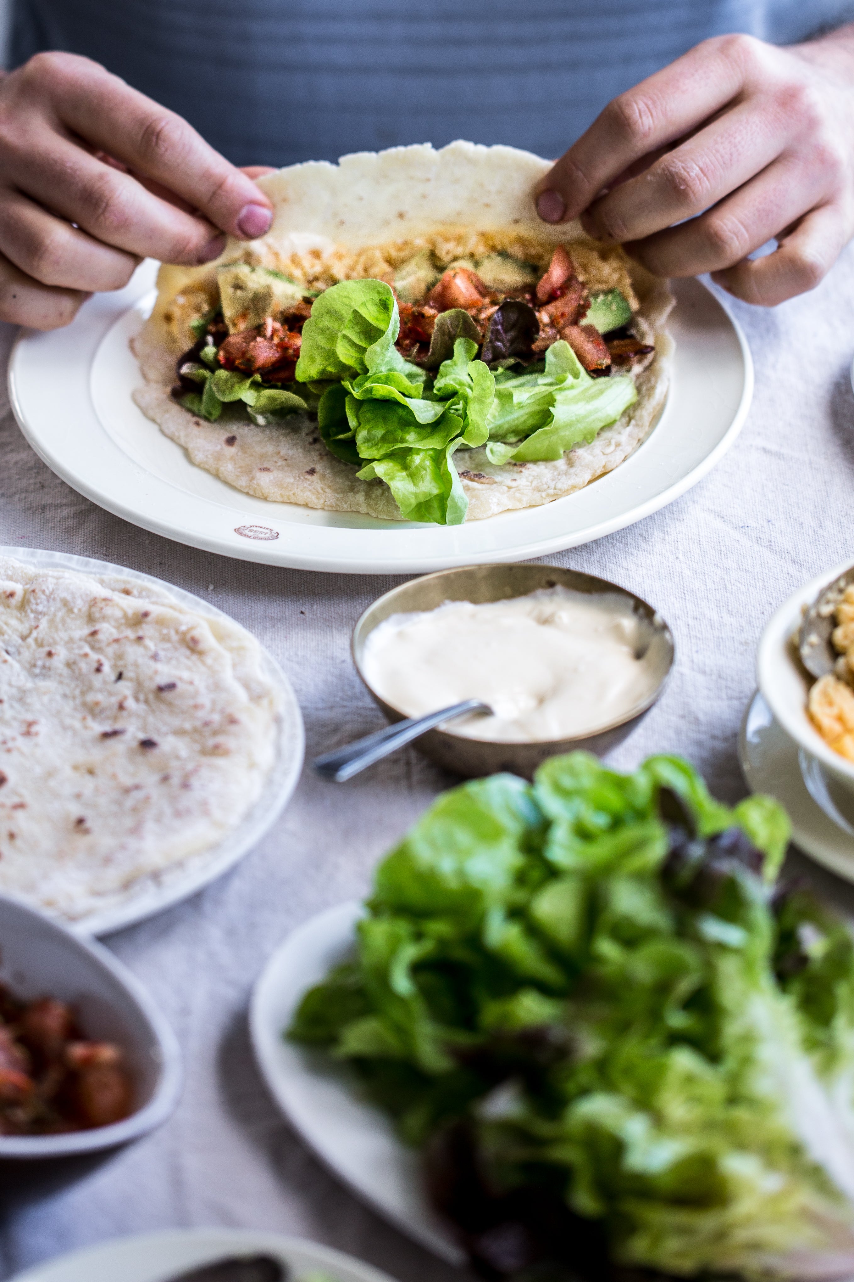 Person assembling a grain free tortilla with ingredients on a table with various food items.