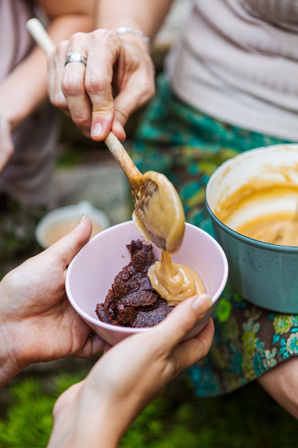 Person spooning dessert into a pink bowl with another person holding it, on a grassy background.