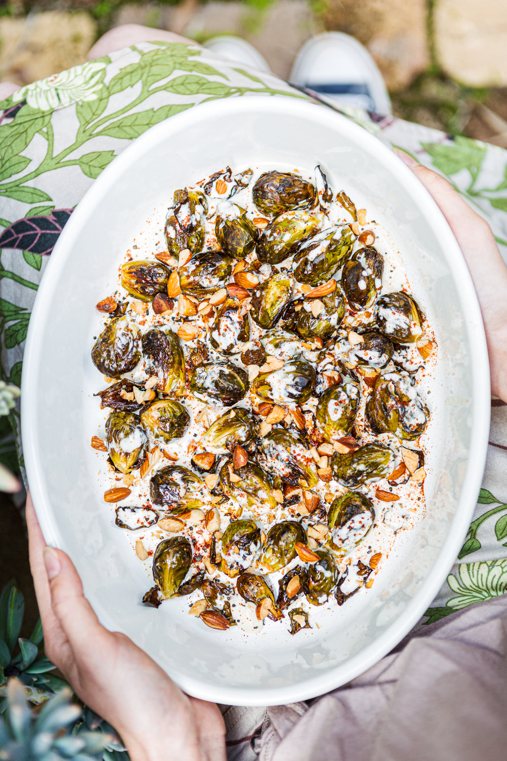 Person holding a white plate with roasted brussels sprouts and seeds outdoors.